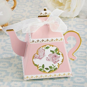 May include: Pink teapot shaped favor box with a white ribbon and floral design. The box is decorated with gold trim and has a white background with pink roses and green leaves.