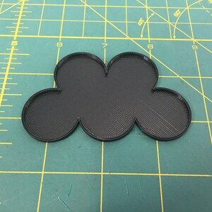 May include: A black plastic cloud-shaped object with five rounded sections. The object is on a green cutting mat with yellow lines.