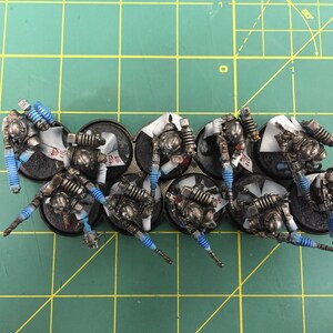 Op de afbeelding: Een groep van tien miniatuurfiguren geverfd in zilver en zwart met blauwe accenten. De figuren staan op ronde zwarte bases.