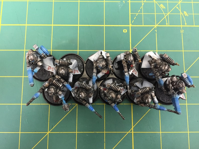 Op de afbeelding: Een groep van tien miniatuurfiguren geverfd in zilver en zwart met blauwe accenten. De figuren staan op ronde zwarte bases.