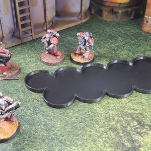 Op de afbeelding: Een set zwarte plastic gamebases voor miniatuurfiguren. De bases zijn met elkaar verbonden in een lange, gebogen lijn. De bases zijn ontworpen om miniatuurfiguren voor tabletop games te houden.