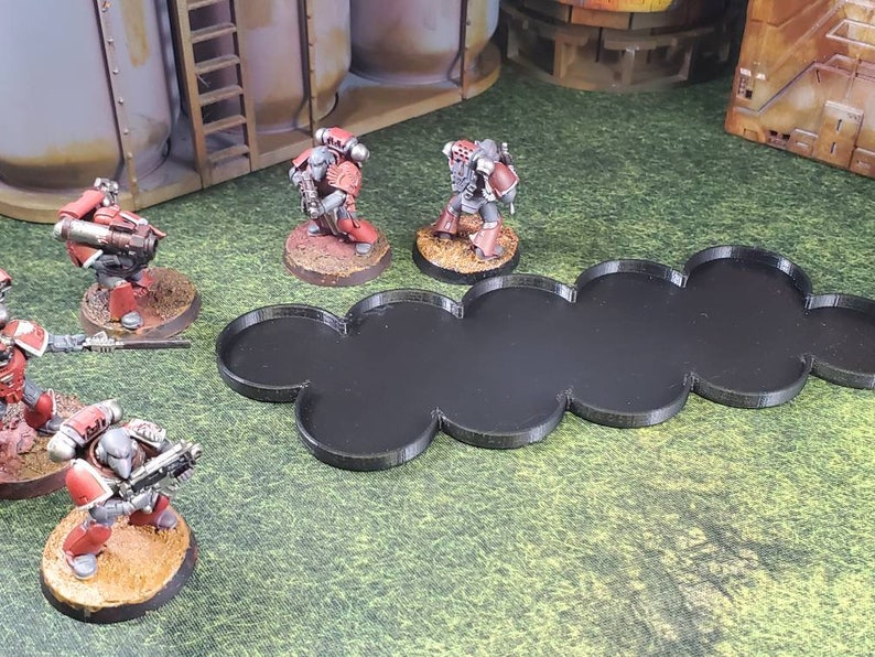 Op de afbeelding: Een set zwarte plastic gamebases voor miniatuurfiguren. De bases zijn met elkaar verbonden in een lange, gebogen lijn. De bases zijn ontworpen om miniatuurfiguren voor tabletop games te houden.