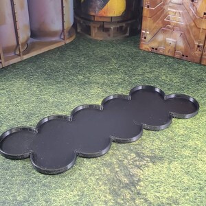 Op de afbeelding: Een zwarte plastic basis met een afgerond, gesegmenteerd ontwerp. De basis bestaat uit zeven verbonden secties, elk met een licht verhoogde rand.