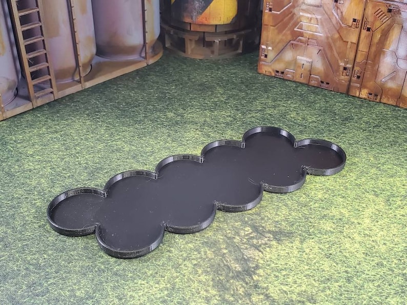 Op de afbeelding: Een zwarte plastic basis met een afgerond, gesegmenteerd ontwerp. De basis bestaat uit zeven verbonden secties, elk met een licht verhoogde rand.