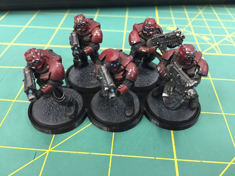 May include: Five red and black miniature figures holding weapons, standing on black bases. The figures are painted with a red and black color scheme.