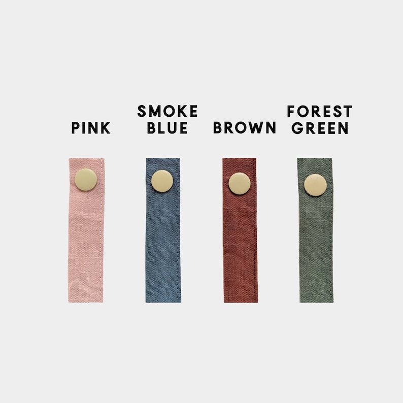 Pu&ograve; includere: Quattro strisce di tessuto rosa, blu fumo, marrone e verde foresta, ciascuna con un bottone color oro. Le parole "PINK", "SMOKE BLUE", "BROWN" e "FOREST GREEN" sono stampate sopra ogni striscia.