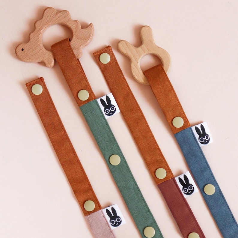 Pu&ograve; includere: Una collezione di clip per ciuccio per bambini in vari colori. Ogni clip presenta un anello di dentizione in legno a forma di dinosauro o coniglietto. I cinturini sono in tonalit&agrave; marrone, verde, blu e rosa, con chiusura a bottone e un'etichetta con un logo di coniglietto.