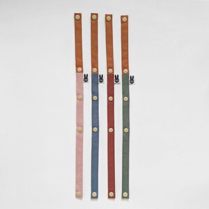Pu&ograve; includere: Cinque cinturini in tessuto colorati con chiusure a scatto. Ogni cinturino ha un colore diverso: rosa, blu, rosso e verde. La parte superiore di ogni cinturino &egrave; in materiale simile alla pelle marrone. Ogni cinturino ha una piccola etichetta con un coniglietto con gli occhiali.