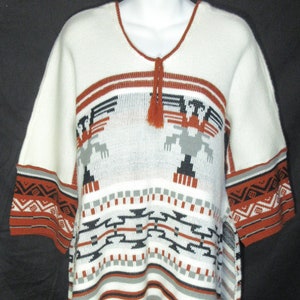 May include: Cream-colored poncho-style sweater with short sleeves and a V-neck. The sweater features geometric patterns in black, gray, and rust-red, with a fringe hem. A rust-red tassel hangs from the neckline. The sleeves have a patterned border.