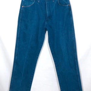 May include: A pair of blue denim jeans, hanging on a white background. The jeans have a classic five-pocket design, with copper rivets and a button closure. The denim is a medium wash, with subtle fading.