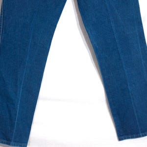 May include: Close-up of blue denim jeans. The jeans have a classic straight-leg fit and feature visible seams down the front and back of the legs. The denim appears to be a medium wash, with subtle variations in colour.