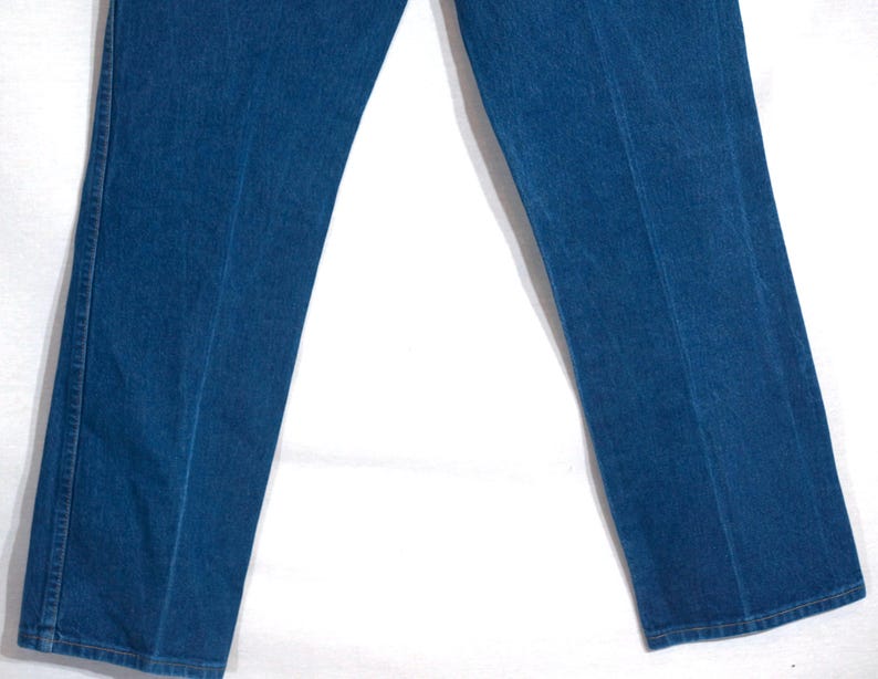 May include: Close-up of blue denim jeans. The jeans have a classic straight-leg fit and feature visible seams down the front and back of the legs. The denim appears to be a medium wash, with subtle variations in colour.