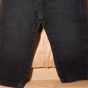 May include: Close-up of black denim jeans. The jeans have a classic five-pocket design with visible stitching along the seams and pockets. The fabric appears to be a dark wash, with a slight sheen.