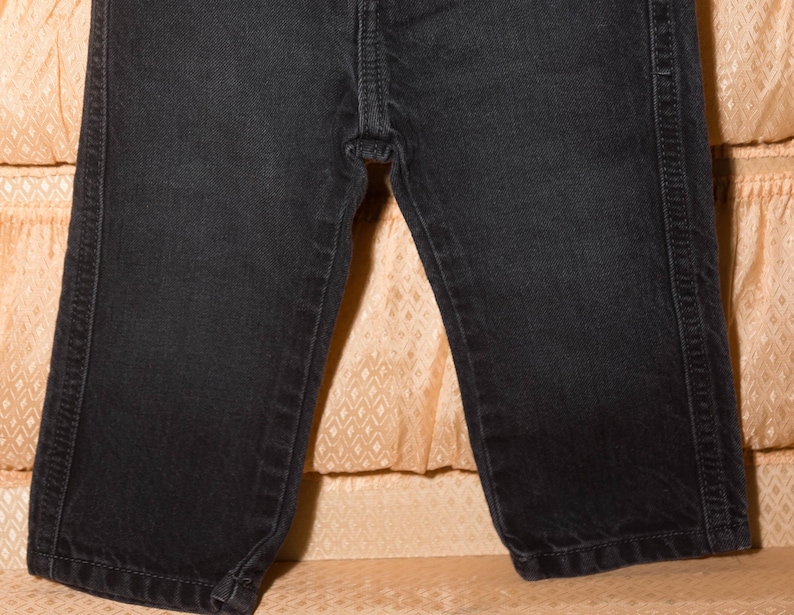 May include: Close-up of black denim jeans. The jeans have a classic five-pocket design with visible stitching along the seams and pockets. The fabric appears to be a dark wash, with a slight sheen.
