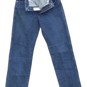 May include: A pair of blue denim jeans, displayed open on a hanger. The jeans have a classic five-pocket design, a button and zipper closure, and a straight leg cut. The denim is a medium wash, and the jeans appear to be vintage.