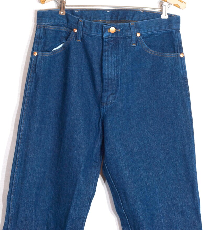 May include: A pair of blue denim jeans with a classic five-pocket design. The jeans feature copper-colored rivets and a button closure. The denim has a medium wash and a straight leg cut.