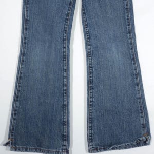 May include: A pair of blue denim jeans with a flared leg design. The jeans have a classic five-pocket style, with visible stitching and a light wash. The hemline is slightly frayed, adding a casual touch to the garment.