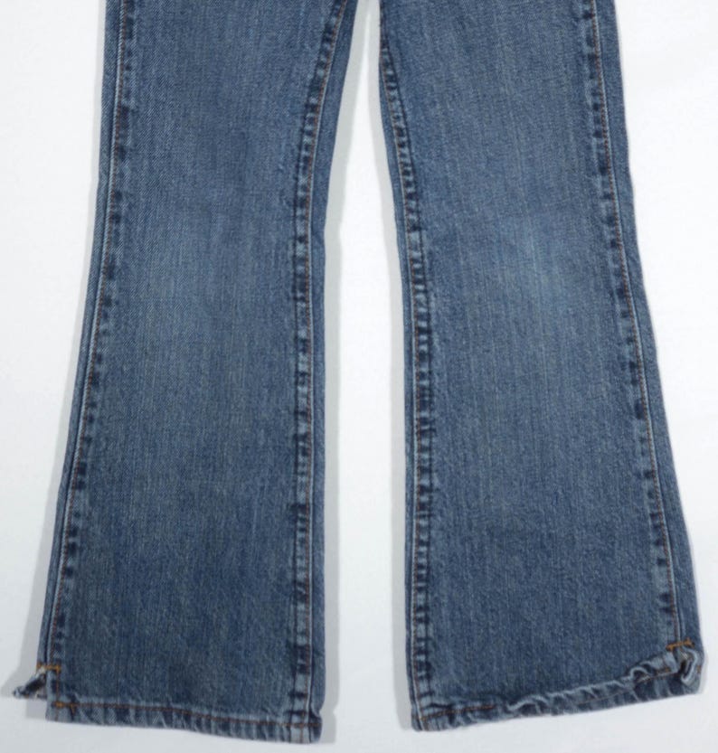 May include: A pair of blue denim jeans with a flared leg design. The jeans have a classic five-pocket style, with visible stitching and a light wash. The hemline is slightly frayed, adding a casual touch to the garment.