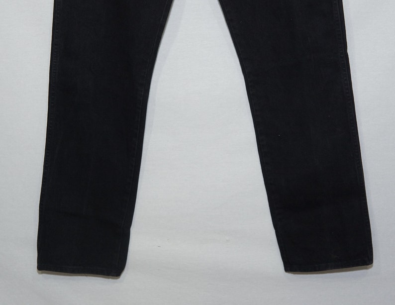 May include: A pair of black denim jeans. The jeans have a classic five-pocket design, with a straight leg cut. The fabric appears to be a medium-weight denim, suitable for year-round wear. The jeans are a solid black color.