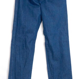 May include: Dark blue denim jeans hanging on a wooden hanger. The jeans are unbuttoned and unzipped, showing the interior lining. The jeans have a classic five-pocket design and a straight leg cut. The denim appears to be a medium weight.