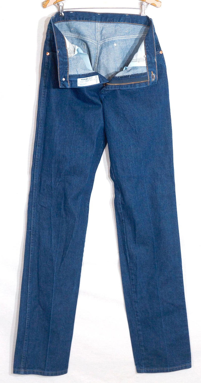 May include: Dark blue denim jeans hanging on a wooden hanger. The jeans are unbuttoned and unzipped, showing the interior lining. The jeans have a classic five-pocket design and a straight leg cut. The denim appears to be a medium weight.