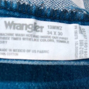 Puede incluir: Primer plano de tejido vaquero azul con etiqueta blanca. La etiqueta dice "Wrangler 13MWZ 34 x 30" e incluye instrucciones de lavado. Fabricado en M&eacute;xico con tejido estadounidense, 100% algod&oacute;n. Cintura 86 cm, largo 76 cm.