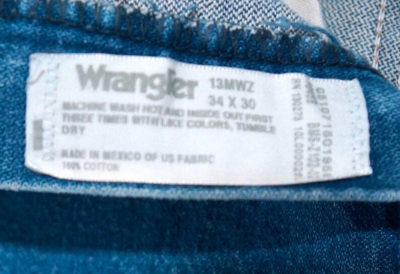 Puede incluir: Primer plano de tejido vaquero azul con etiqueta blanca. La etiqueta dice "Wrangler 13MWZ 34 x 30" e incluye instrucciones de lavado. Fabricado en M&eacute;xico con tejido estadounidense, 100% algod&oacute;n. Cintura 86 cm, largo 76 cm.
