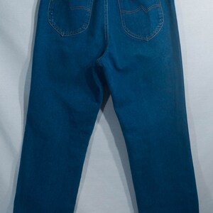 May include: Blue denim jeans with a high waist, featuring back pockets with decorative stitching and a small, rectangular brand label. The jeans are displayed on a hanger against a plain background.