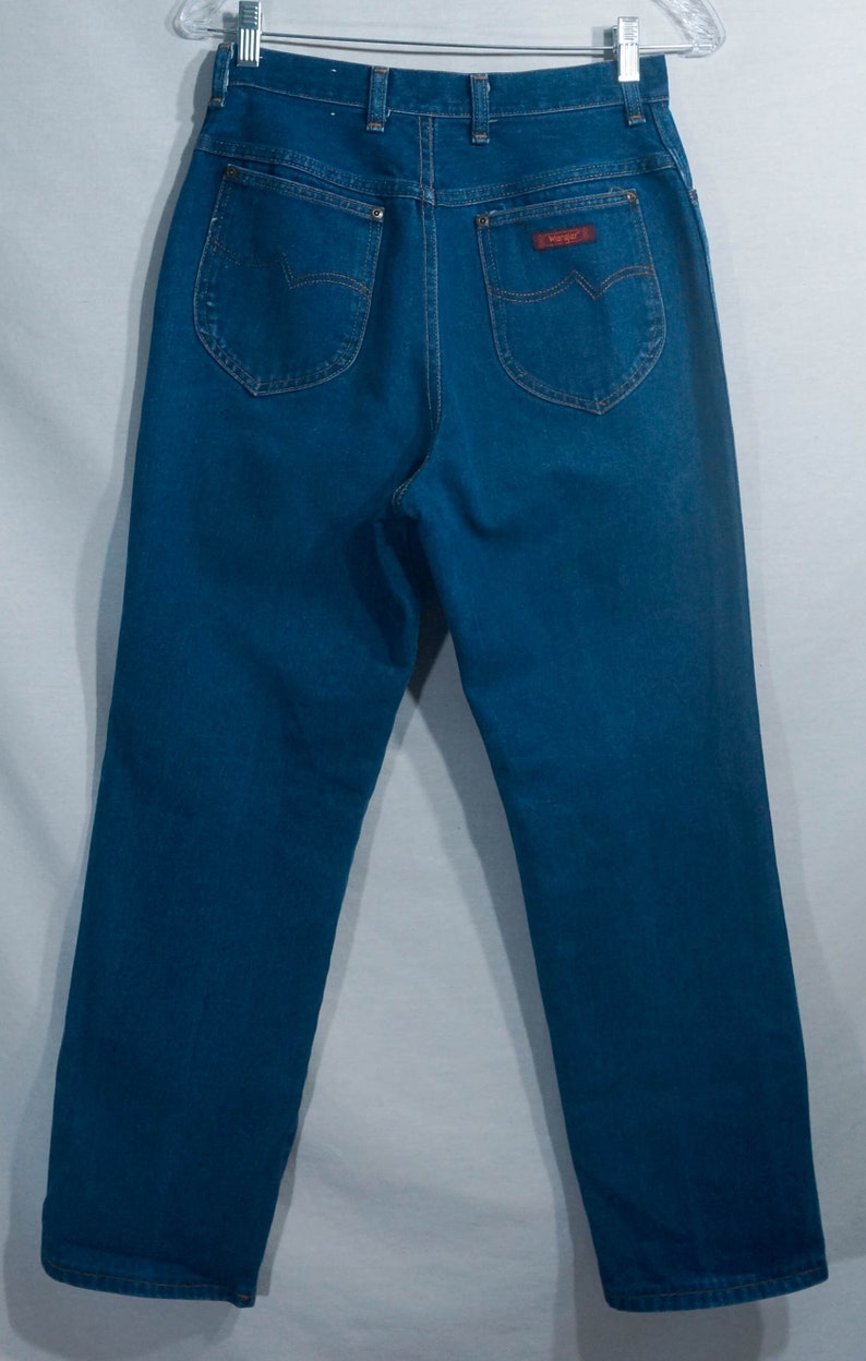 May include: Blue denim jeans with a high waist, featuring back pockets with decorative stitching and a small, rectangular brand label. The jeans are displayed on a hanger against a plain background.