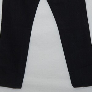 May include: A pair of black pants. The pants are straight-legged and made of a solid black fabric. The image shows the lower portion of the pants, from the knees down, against a white background. The pants are neatly pressed.