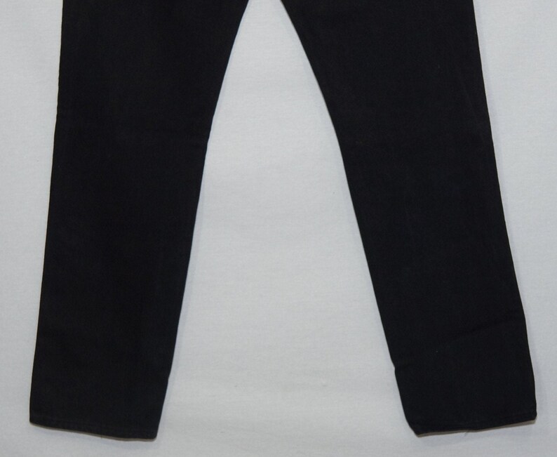 May include: A pair of black pants. The pants are straight-legged and made of a solid black fabric. The image shows the lower portion of the pants, from the knees down, against a white background. The pants are neatly pressed.