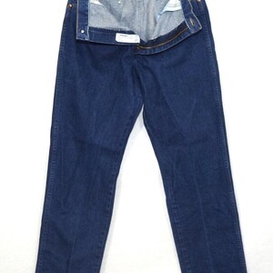 May include: Dark blue denim jeans hanging on a metal hanger. The jeans are unbuttoned and unzipped, revealing the interior lining. The jeans have a classic five-pocket design and a straight leg cut.
