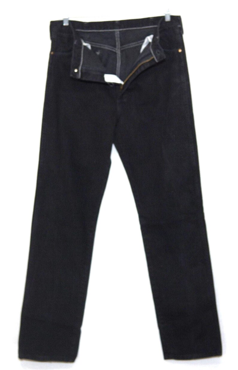 May include: Black denim jeans with a button and zipper closure. The jeans are hanging on a hanger against a white background. The jeans have a classic five-pocket design and a straight leg.