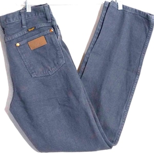May include: Dark blue Wrangler jeans with a classic straight-leg fit. Features a brown leather patch on the back pocket and brass rivets. The Wrangler logo is visible on the back pocket and above the right back pocket. A timeless denim staple.
