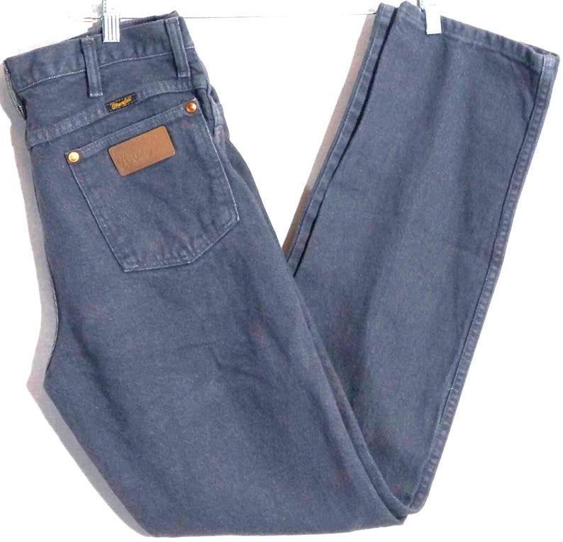 May include: Dark blue Wrangler jeans with a classic straight-leg fit. Features a brown leather patch on the back pocket and brass rivets. The Wrangler logo is visible on the back pocket and above the right back pocket. A timeless denim staple.