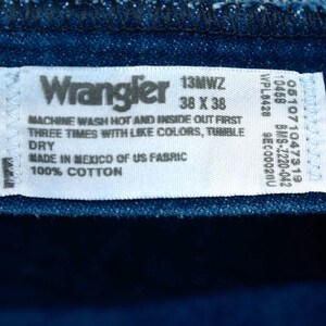 May include: Close-up of a blue denim fabric with a white label. The label reads "Wrangler" and includes washing instructions, size 38 x 38, and fabric details. The fabric is 100% cotton and made in Mexico.