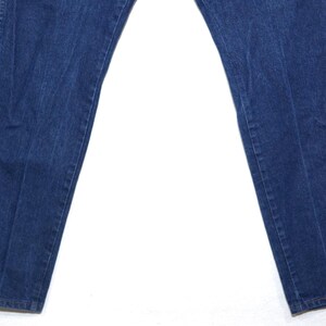 May include: Dark blue denim jeans, featuring a classic five-pocket design and a straight leg cut. The denim has a slightly faded appearance, with subtle wear marks. The jeans are laid flat on a white surface.