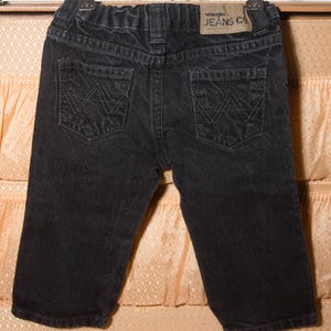 May include: Black denim Wrangler Jeans Co. shorts with two back pockets featuring the Wrangler logo. The shorts have a faded appearance and a small leather patch with the brand name.