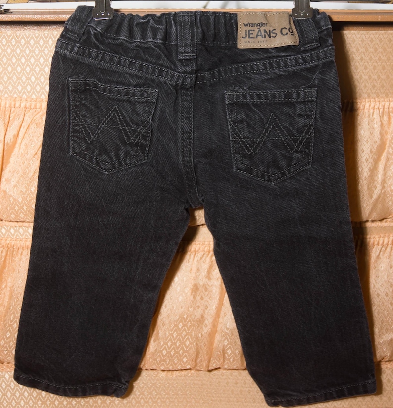 May include: Black denim Wrangler Jeans Co. shorts with two back pockets featuring the Wrangler logo. The shorts have a faded appearance and a small leather patch with the brand name.