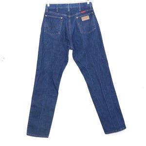 May include: Dark blue denim jeans with a classic five-pocket design. The jeans have a straight leg cut and a brown leather patch with the brand name on the back. The jeans are hanging on a metal hanger.