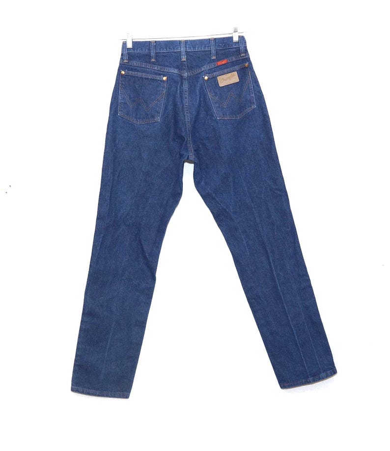 May include: Dark blue denim jeans with a classic five-pocket design. The jeans have a straight leg cut and a brown leather patch with the brand name on the back. The jeans are hanging on a metal hanger.