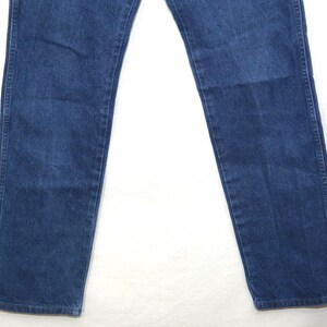 May include: A pair of blue denim jeans. The jeans have a classic five-pocket design, with a straight leg cut. The denim has a medium wash, with some fading and wear visible. The jeans are made of a durable cotton blend.