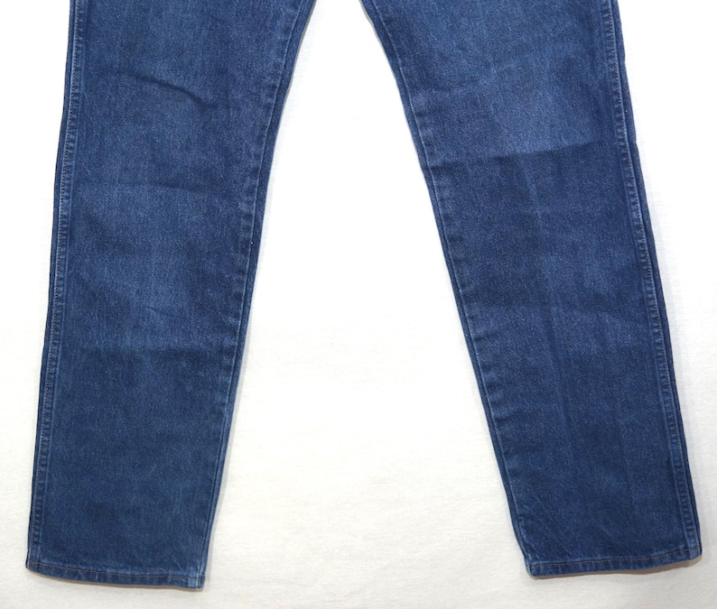 May include: A pair of blue denim jeans. The jeans have a classic five-pocket design, with a straight leg cut. The denim has a medium wash, with some fading and wear visible. The jeans are made of a durable cotton blend.