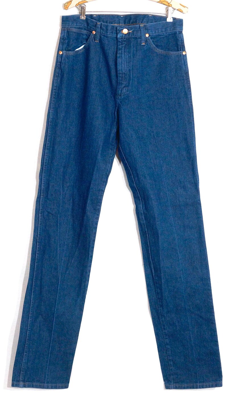 May include: A pair of classic blue denim jeans. The jeans have a straight leg cut, five pockets, and a button and zipper closure. The jeans are hanging on a wooden hanger against a white background.