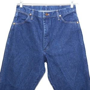 May include: A close-up shot of blue denim jeans. The jeans feature a classic five-pocket design, a button closure, and copper-coloured rivets. The jeans are suspended from a metal hanger against a white backdrop.