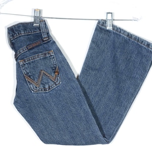 May include: Blue denim jeans with a classic five-pocket design, hanging from a metal hanger. The jeans feature a brown and gold stitched back pocket with a distinctive 'W' logo. The jeans are made of a durable denim material.