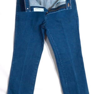 May include: A pair of blue denim jeans, unbuttoned and hanging from a metal hanger. The jeans have a classic five-pocket design and a straight leg cut. The denim is a medium wash, and the jeans appear to be unworn.