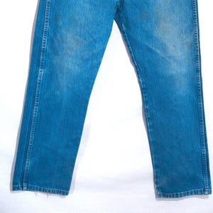 Puede incluir: Un par de vaqueros azules descoloridos. Los vaqueros tienen un dise&ntilde;o cl&aacute;sico de cinco bolsillos, con un corte recto. El denim muestra signos de desgaste y decoloraci&oacute;n, d&aacute;ndole un aspecto vintage. Los vaqueros no est&aacute;n dobladillos.