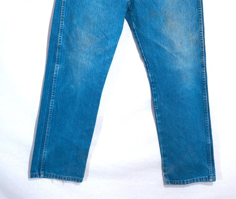 Puede incluir: Un par de vaqueros azules descoloridos. Los vaqueros tienen un dise&ntilde;o cl&aacute;sico de cinco bolsillos, con un corte recto. El denim muestra signos de desgaste y decoloraci&oacute;n, d&aacute;ndole un aspecto vintage. Los vaqueros no est&aacute;n dobladillos.