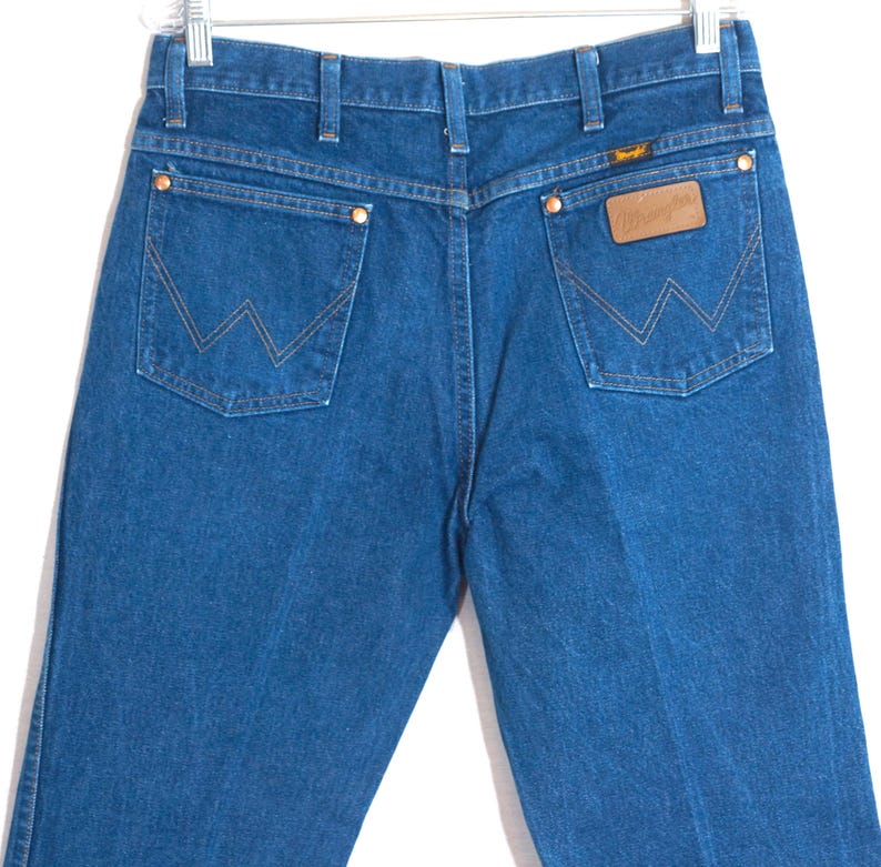 May include: Blue denim jeans with the Wrangler logo on the back pocket. The jeans have a classic five-pocket design with copper rivets and a straight leg. The back pockets feature the signature Wrangler "W" stitching.